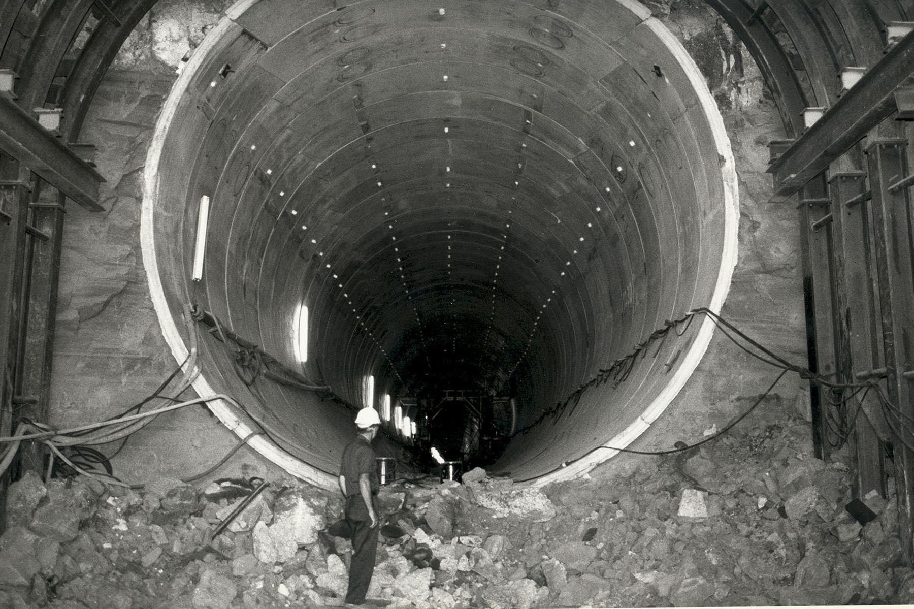 close up picture of an underground water canal under construction. there is a man standing at the edge of the built canal staring into it.