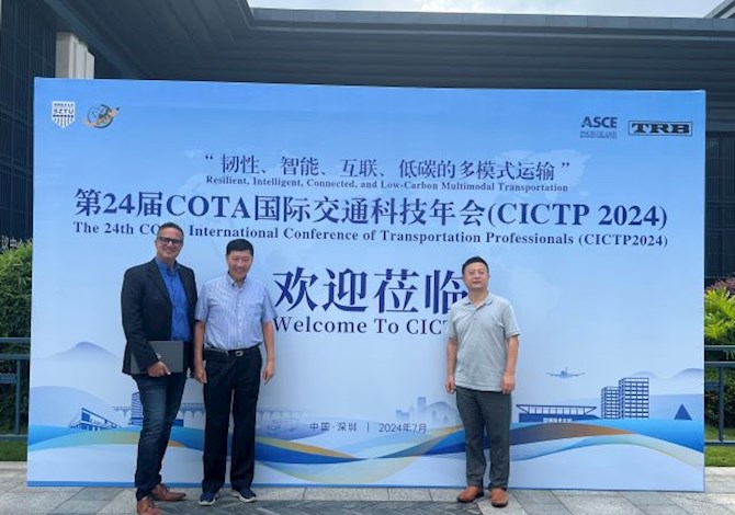 Three people are standing in front of a sign smiling at the camera