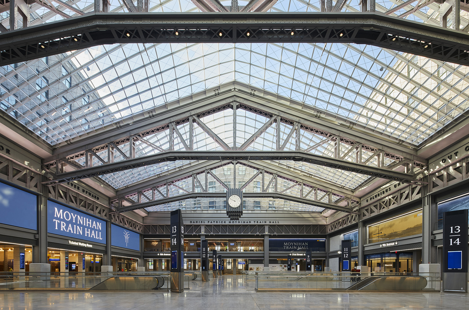 glass-topped room with steel supports showing. there is a big clock hanging from the center of the hall.