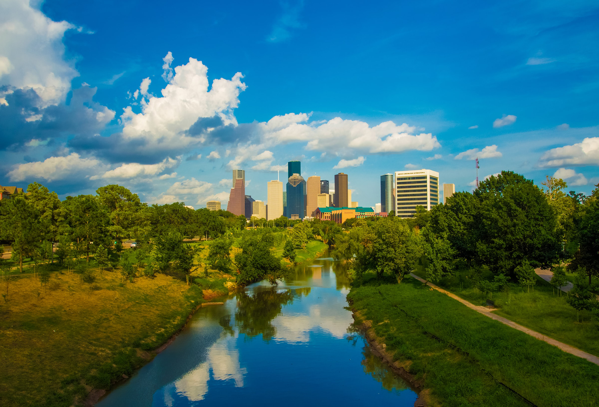 photo showing the Houston skyline in the background and a waterway surrounded by trees in the foreground lead 