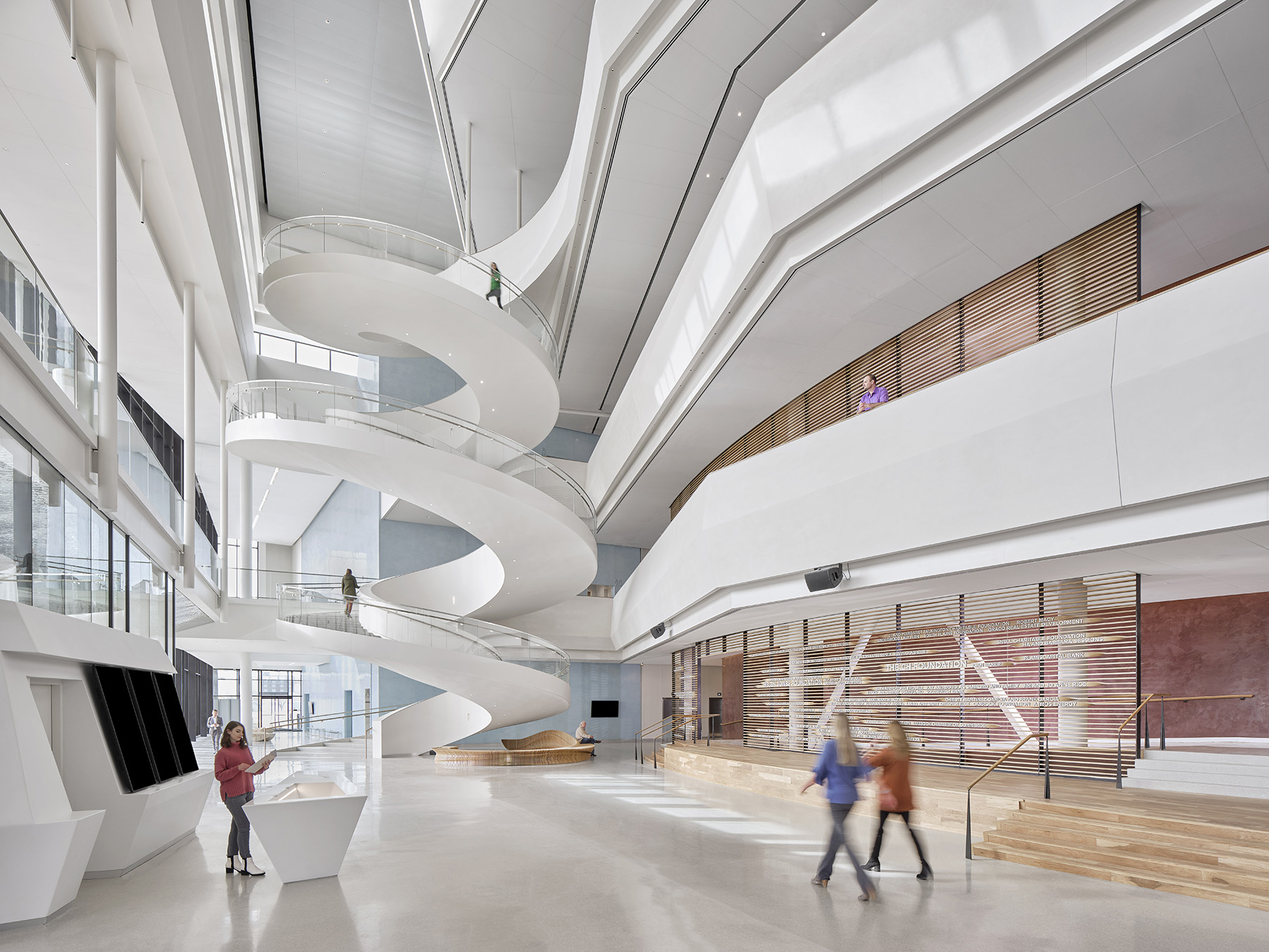 people walking in a multistory open space. there is a spiral staircase in the background.