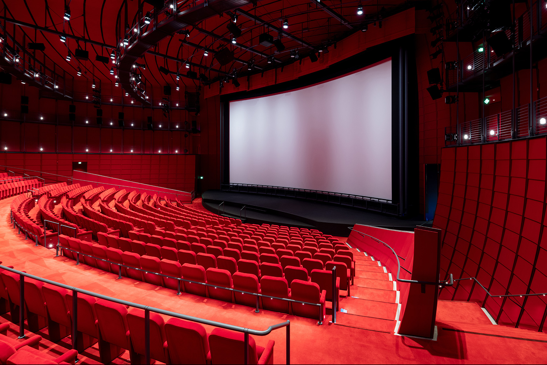 Room full of red seats and red carpet and a large screen in the middle