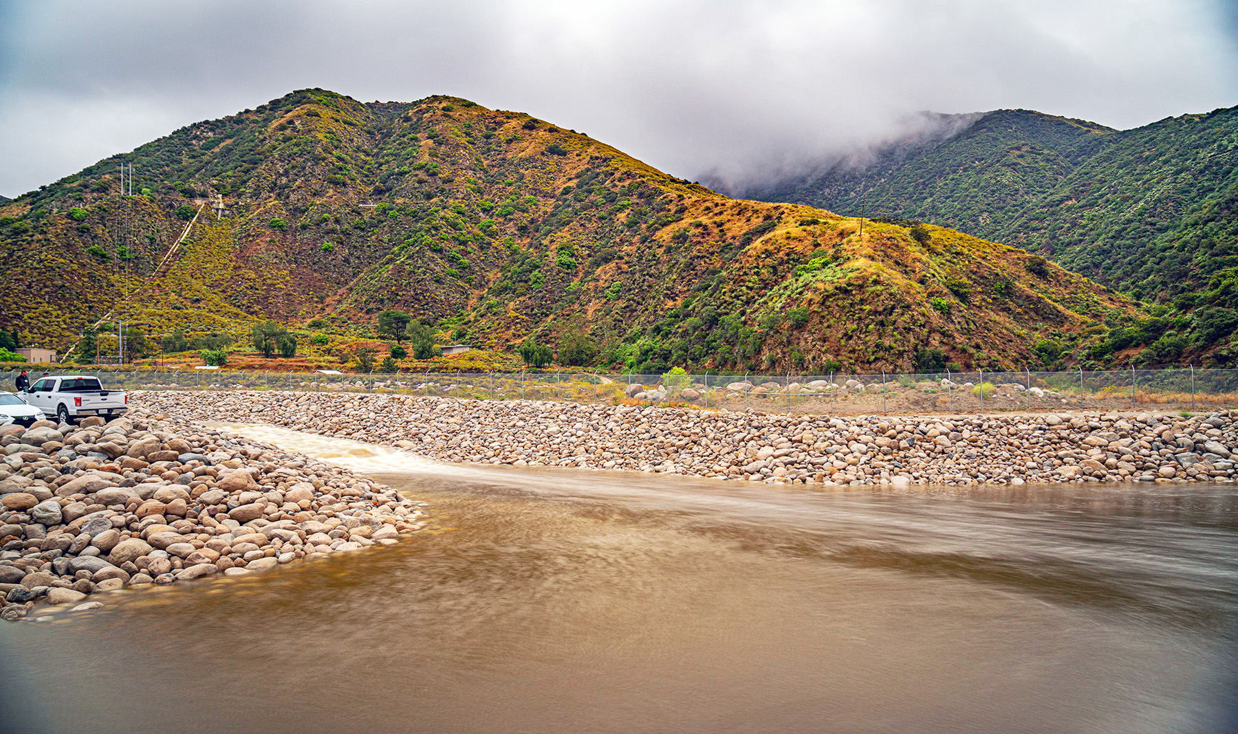 A large hill is in the background and in the foreground is groundwater flowing over rocks. 