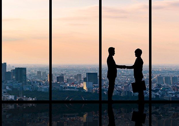 A city skyline is highlighted against the sunset. Two executives are shown shaking hands in silhouette. 