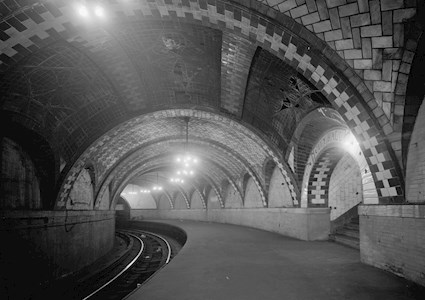 Photograph shows the interior of a subway station—its tracks and decorative ceiling tiles. 