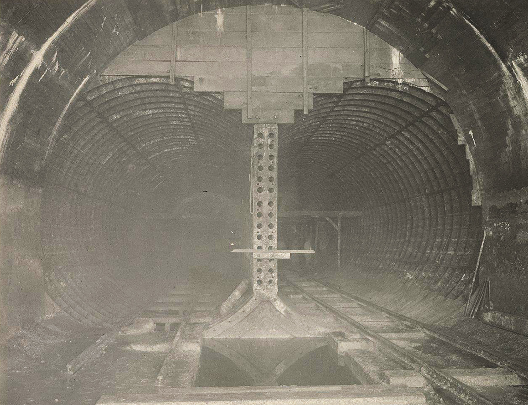 Photograph shows the interior of a subway tunnel with its parallel steel tubes and tracks. 
