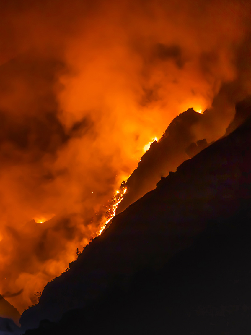 A night-time wildfire is burning down a hillside. 