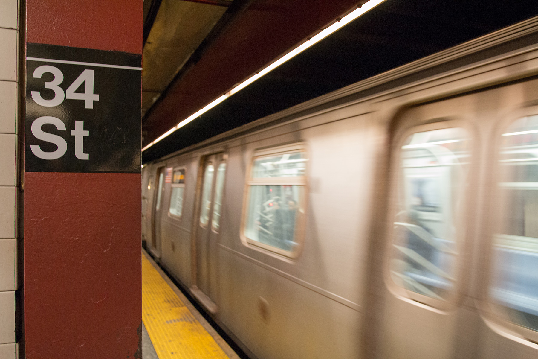 A white, blurry subway car leaves a yellow platform. 