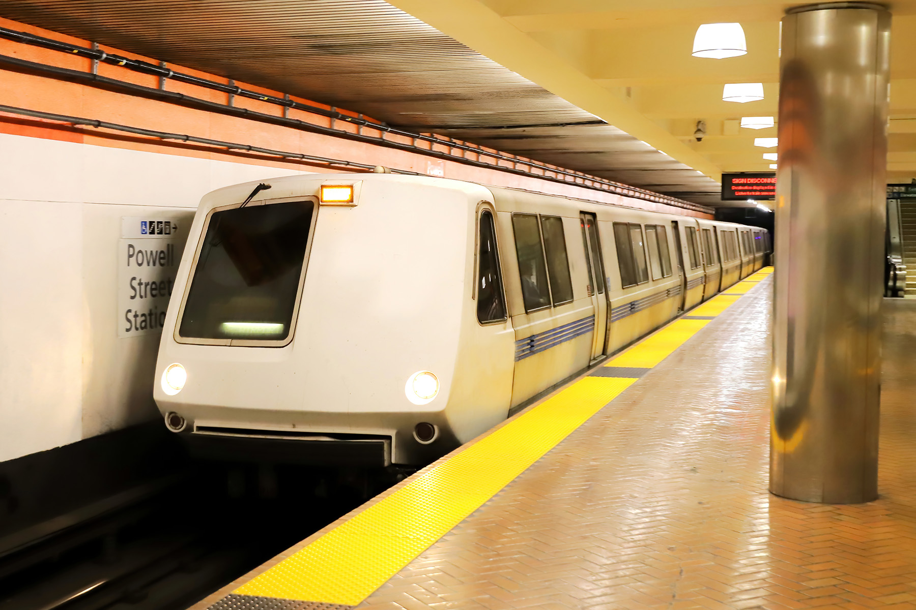 A white subway car sits at an empty indoor platform at Powell Street Station. 