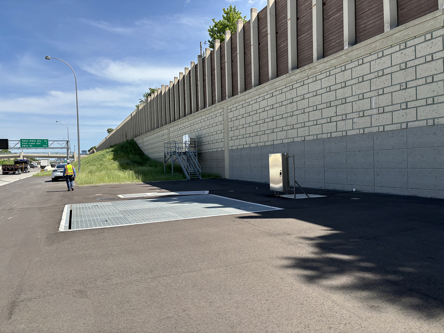 Image shows the a paved surface with a large grate in it. A wall is in the background. 