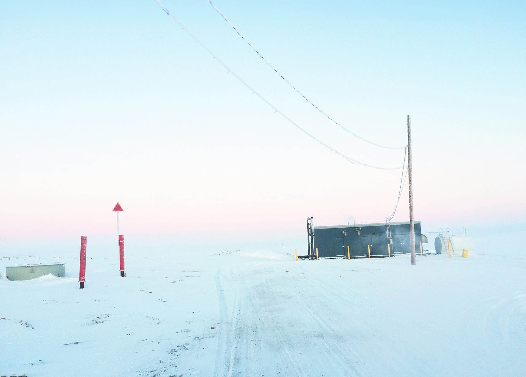 A frozen landscape surrounds a small building and a pole with wires. 