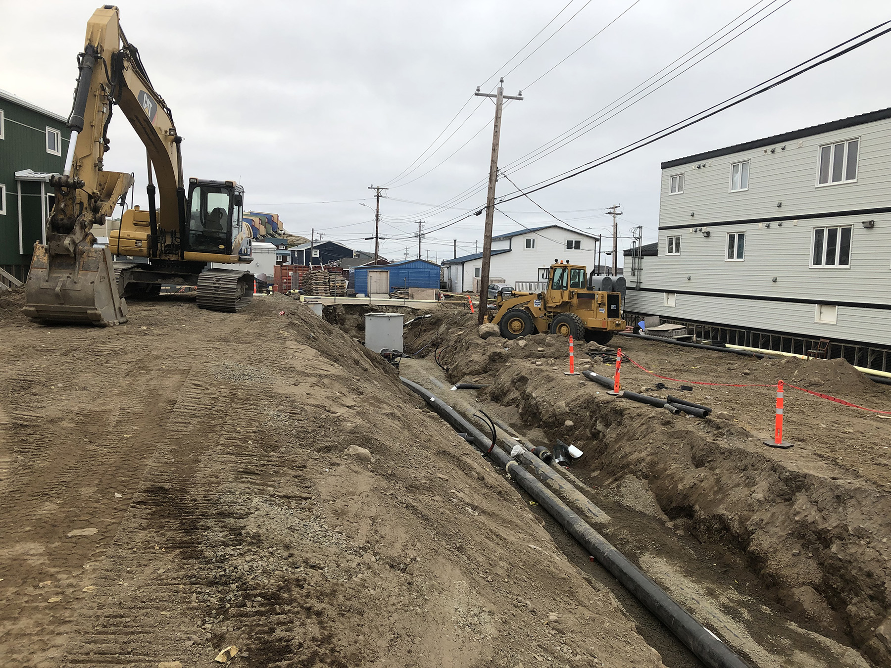 An insulated pipe is being constructed in a trench, with construction equipment nearby.