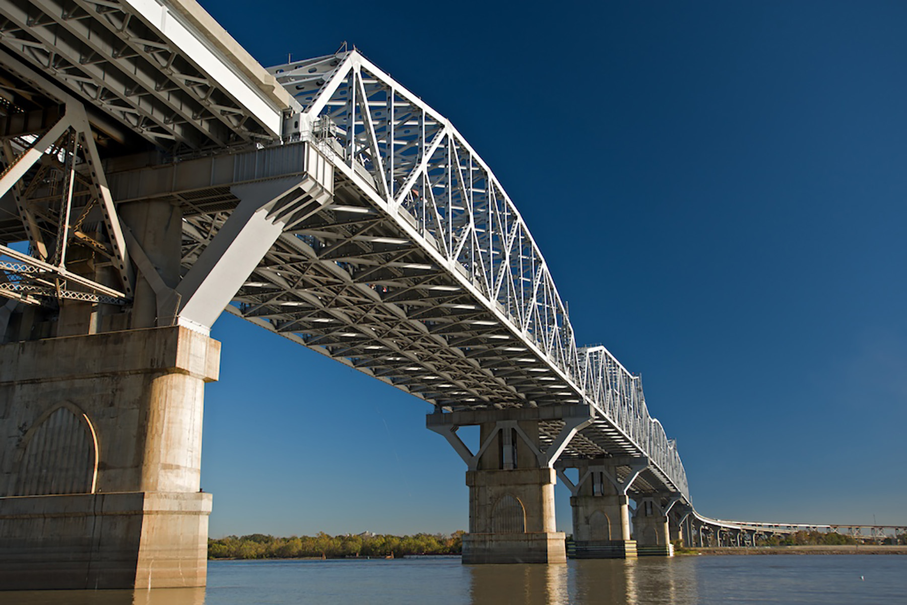 Photo shows a steel bridge with concrete piers. The bridge spans a river. 