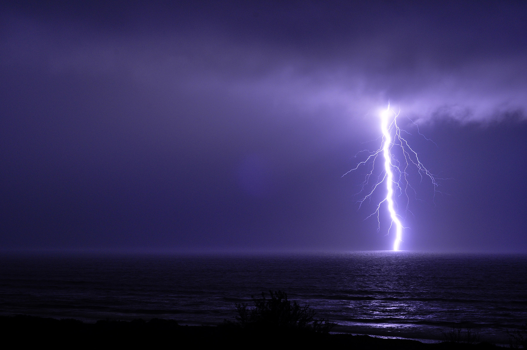 The photograph shows a large lightning strike over water. 