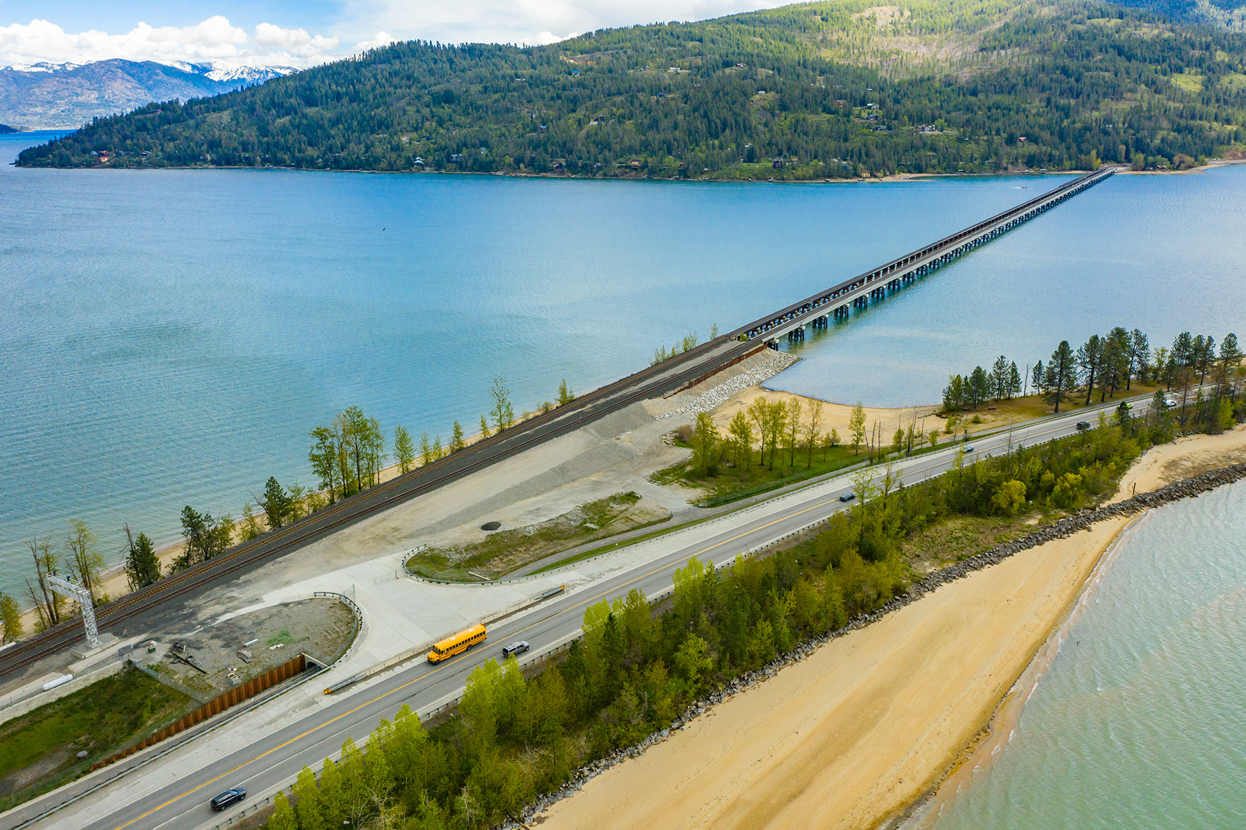 A railroad track and bridge crosses Lake Pend Orielle. Trees line the background and foreground. 