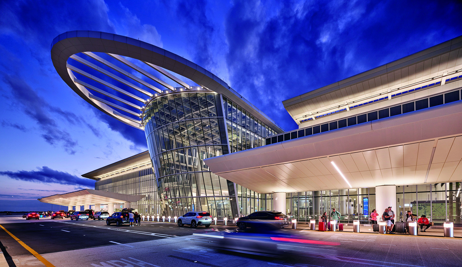 A multistory glass structure with a round arch on the top connects to a concrete structure. 