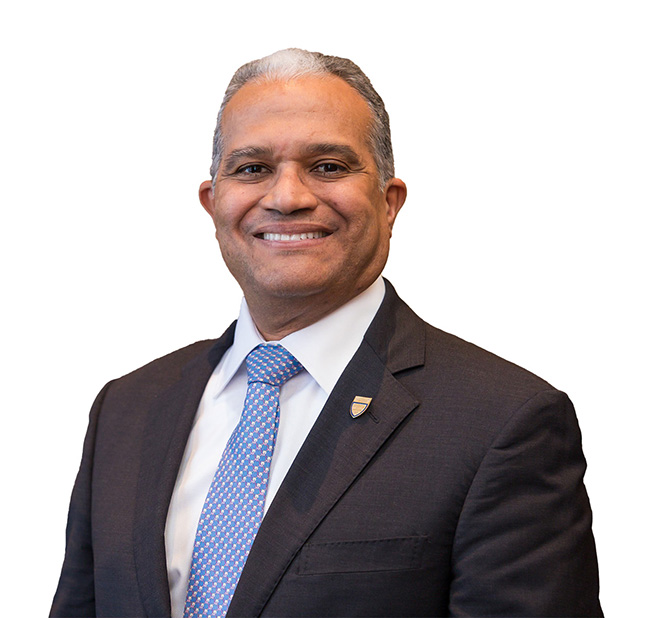 Man in blue jacket, white shirt, and white polka dot tie smiles at the camera. 