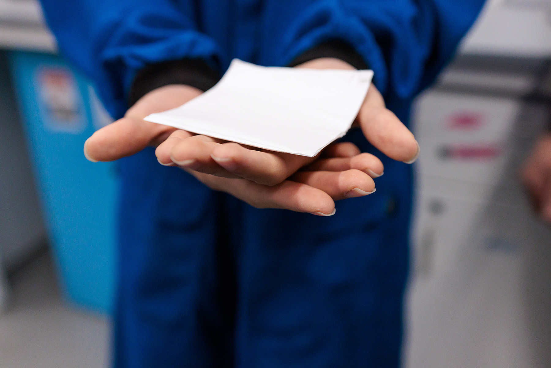 Photograph shows a woman holding a thin white square of material. 