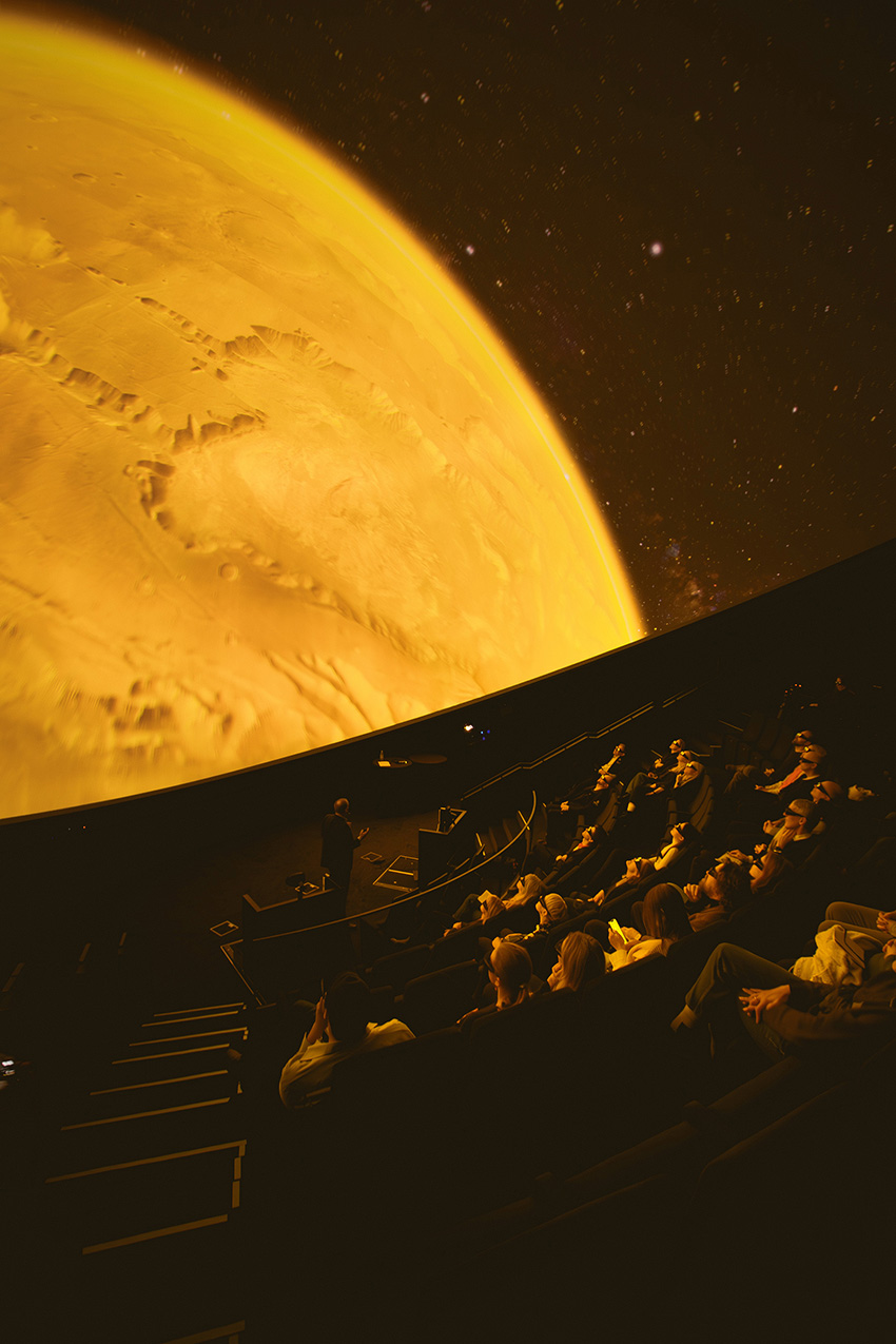 Within the domed arena, the audience watches a film about space. 