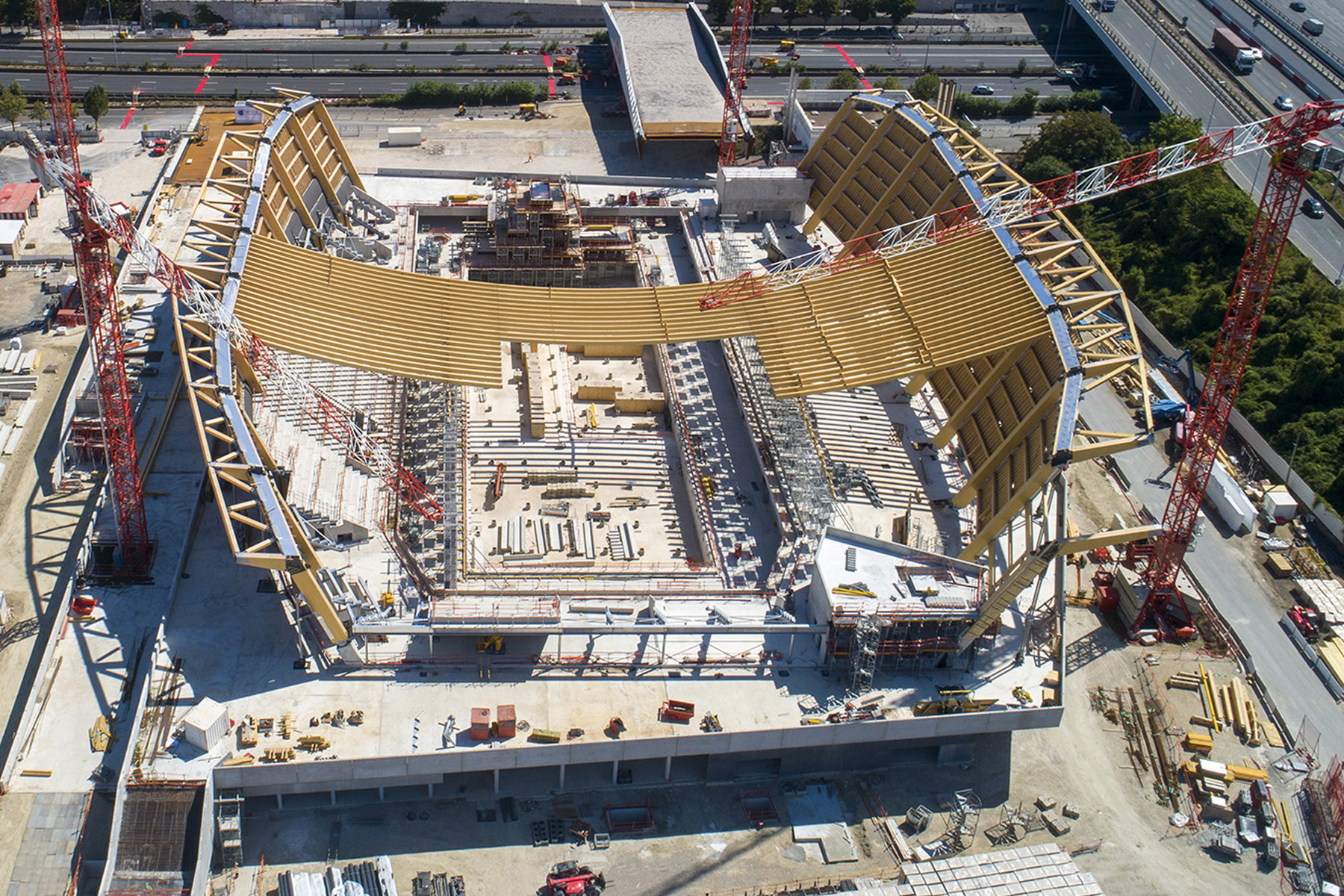 An aerial view of the construction site shows the middle of the wooden roof installed. 