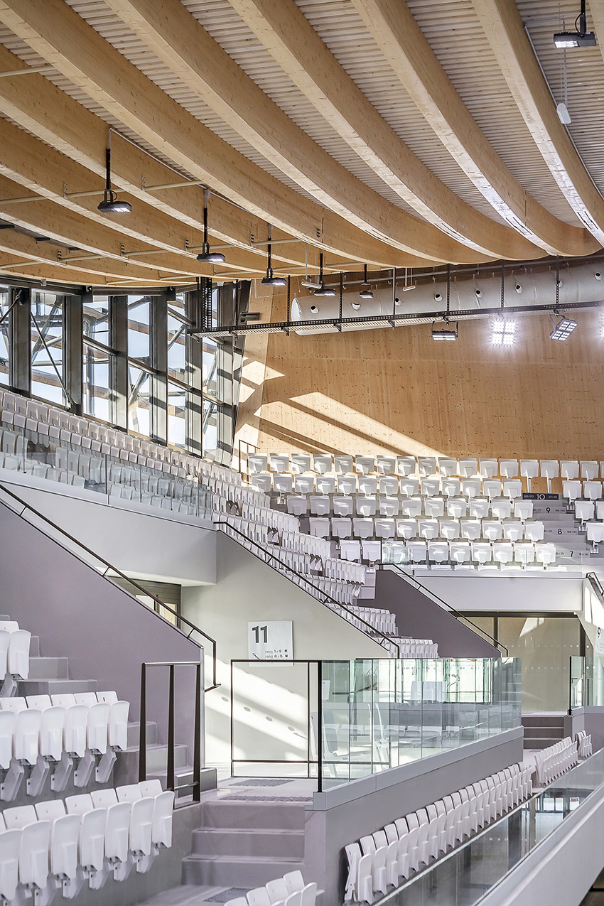 White seats that are folded up in place are in rows on an upper and lower deck next to the pool. 