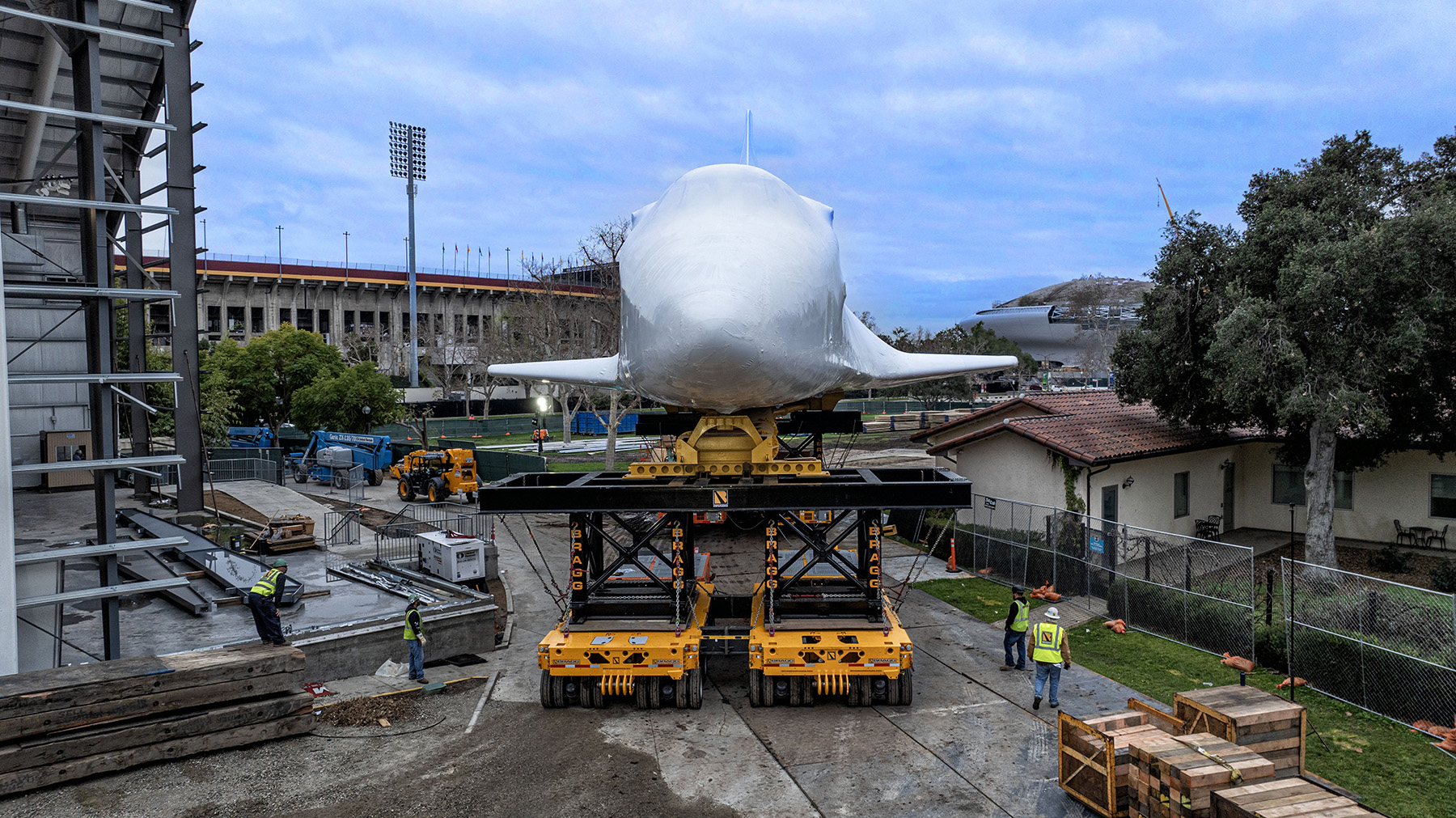 Wrapped in a protective white material, Endeavour is moved along a road on wheeled transporters. 