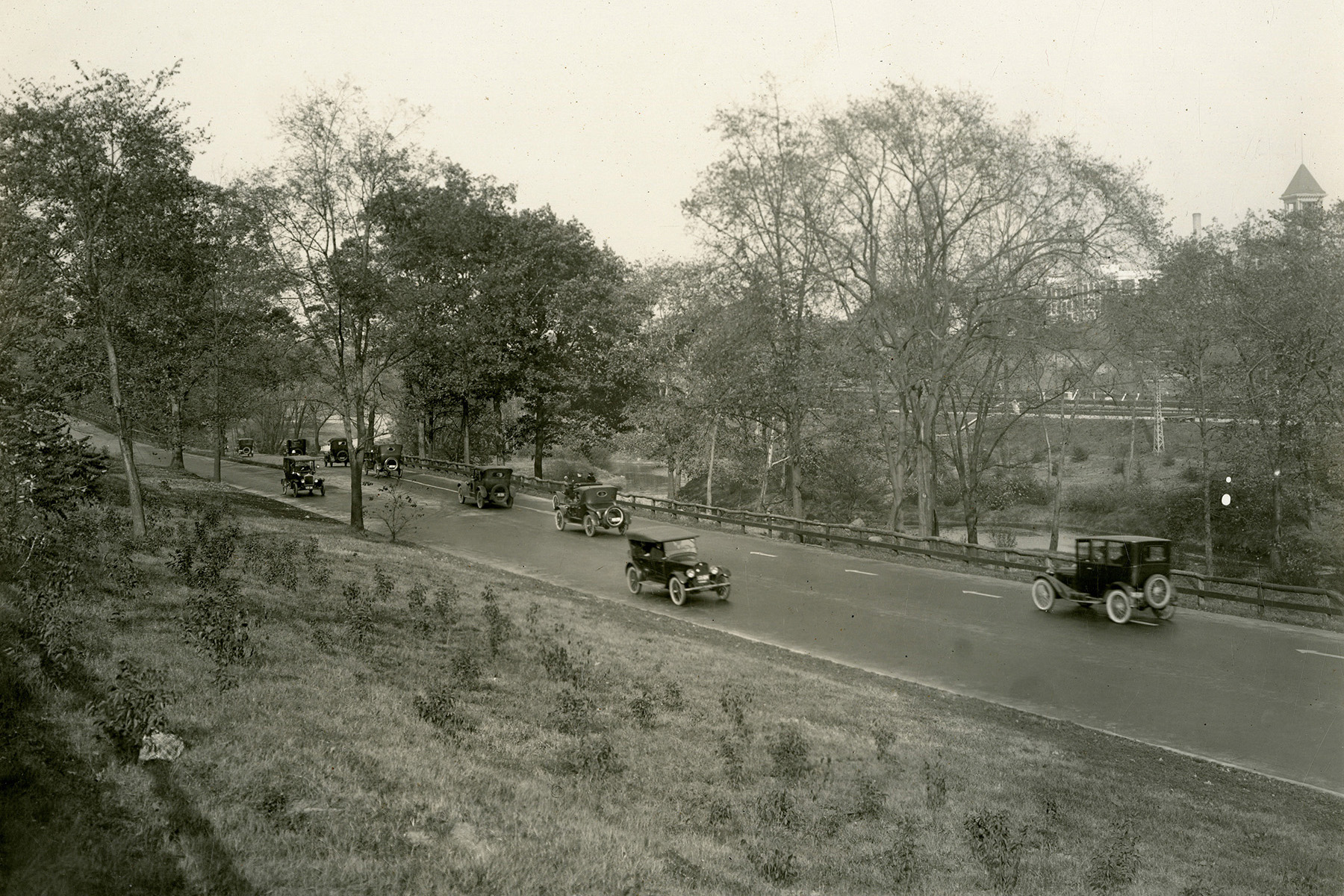 Black and white photograph of the Bronx River Parkway. Cars travel a parkway that sits next to a body of water. 