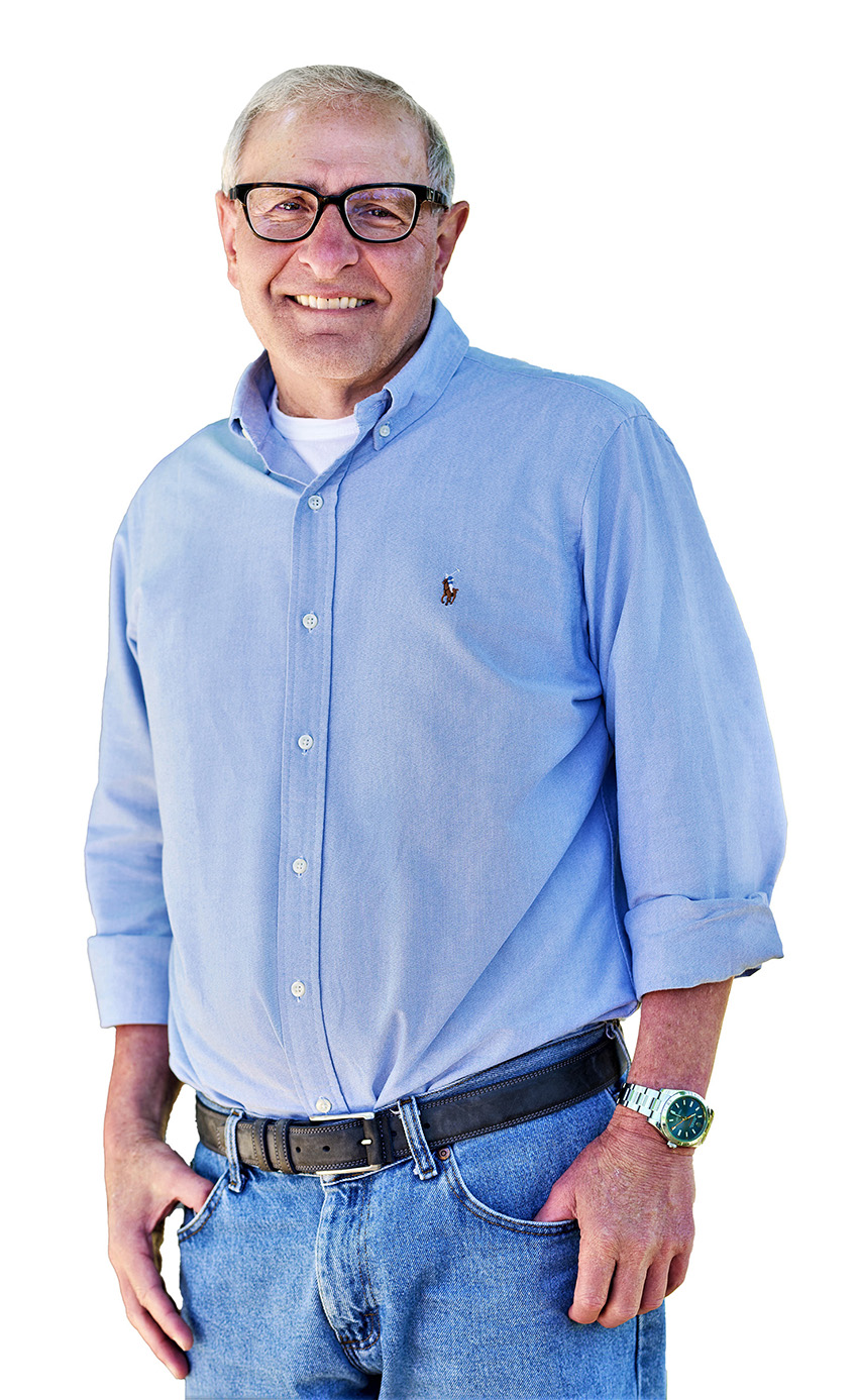 A man wearing glasses and a blue, buttoned-down shirt smiles at the camera. 