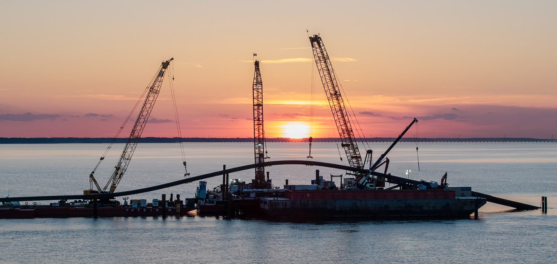 the sun sets over a body of water featuring a boat and construction equipment the sun sets over a body of water featuring a boat and construction equipment