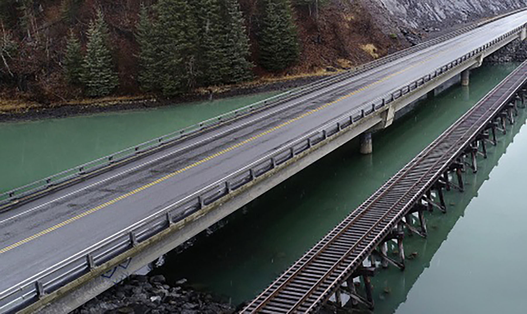 a rail along a body of water with a highway above it