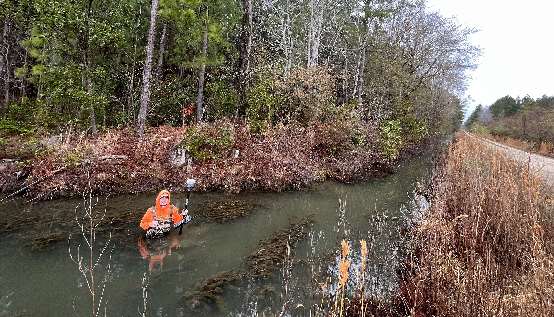 person wades in water with surveying equipment